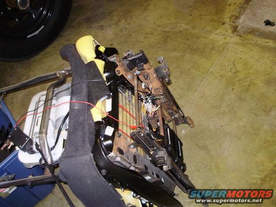 Car seat mechanism with exposed wiring and yellow foam padding, viewed from the side