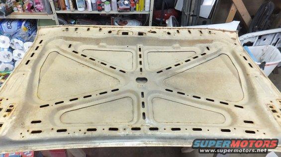 Underside of a cream-colored car hood with reinforcement ribs and stamped openings