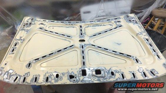 Underside of a cream-colored car hood with metal bracing and repair work
