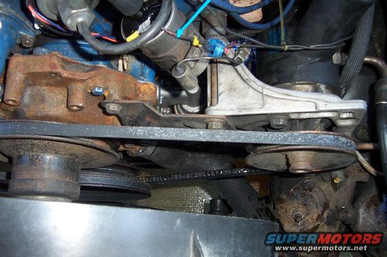 Close-up of engine pulleys and belts, with a rusty water pump housing