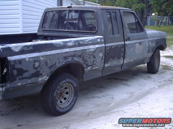 Side view of a 1989 Ford F-150 pickup truck in primer, undergoing body work