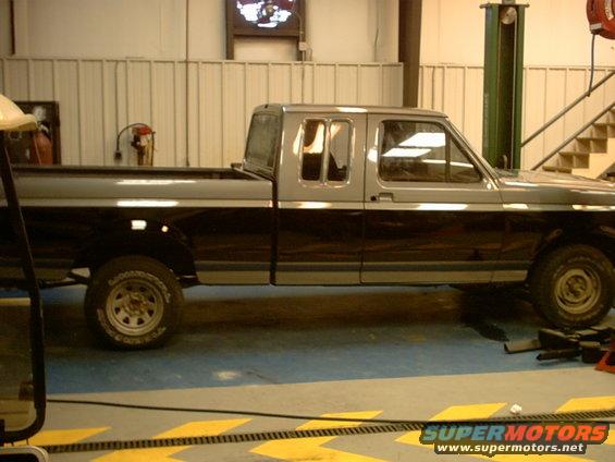 Two-tone gray and black Ford F-150 pickup truck, side view, in a garage
