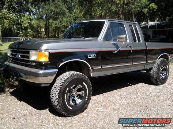 Two-tone grey and black Ford F-150 pickup truck with red pinstriping, lifted suspension, and off-road tires
