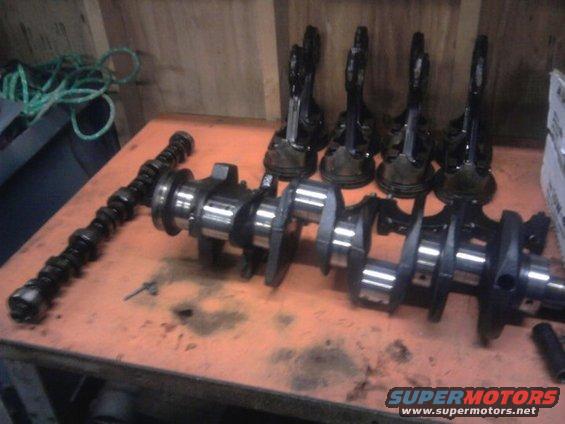 Crankshaft and pistons laid out on an orange surface. A camshaft is to the left