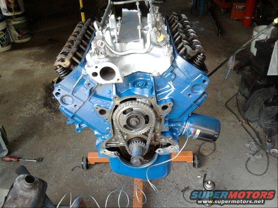 Ford V8 engine block painted blue, showing timing chain and gears. Engine is on an orange stand