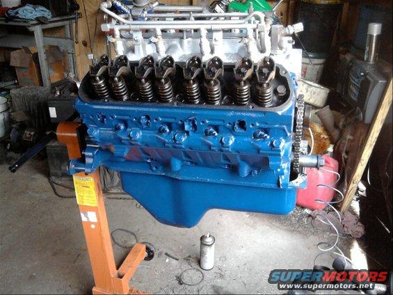 blue V8 engine on an orange engine stand, showing the valve train and timing chain