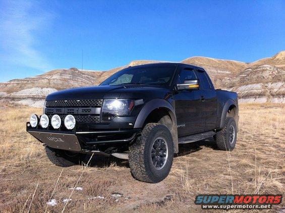Black 2010 Ford F-150 Raptor pickup truck with aftermarket bumper and lights parked in a dry, hilly landscape