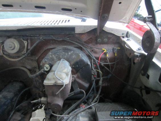 Engine bay with brake fluid reservoir, wiring, and fuse box. Hood hinges visible