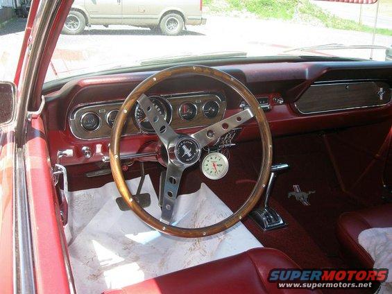 1965 Ford Mustang interior with wood-rimmed steering wheel, red seats, and dashboard gauges