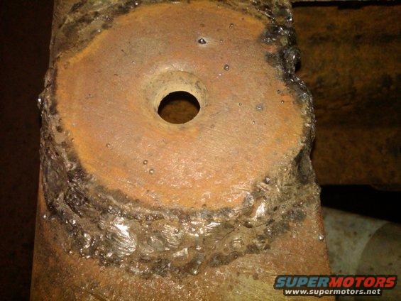 Close-up of a heavily rusted metal bracket with a central hole and visible weld marks