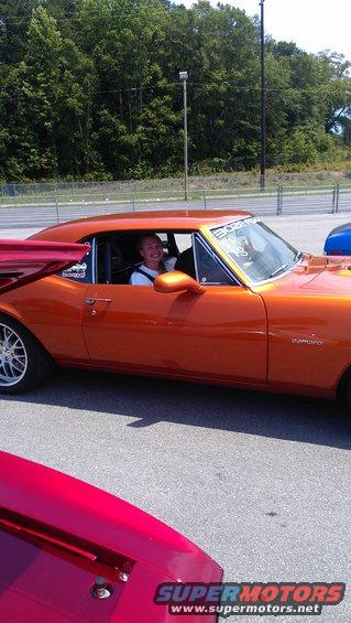 Orange 1969 Camaro with a person in the driver's seat, another red car in the foreground