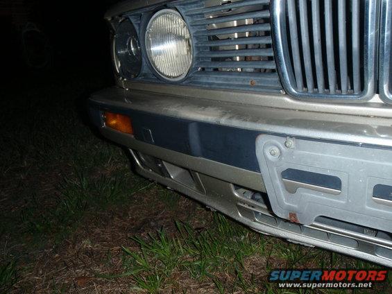 BMW front bumper with orange turn signal, chrome grille, and license plate bracket. Gold and blue paint visible