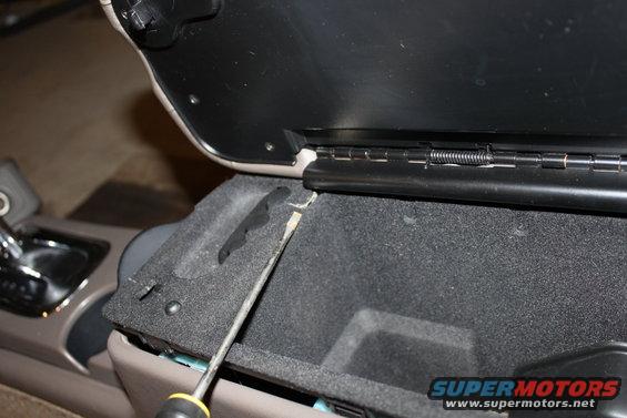 Center console compartment being pried open with a screwdriver