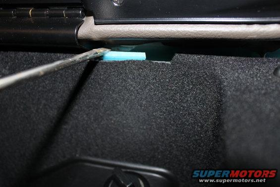 Screwdriver prying blue foam insulation inside car interior