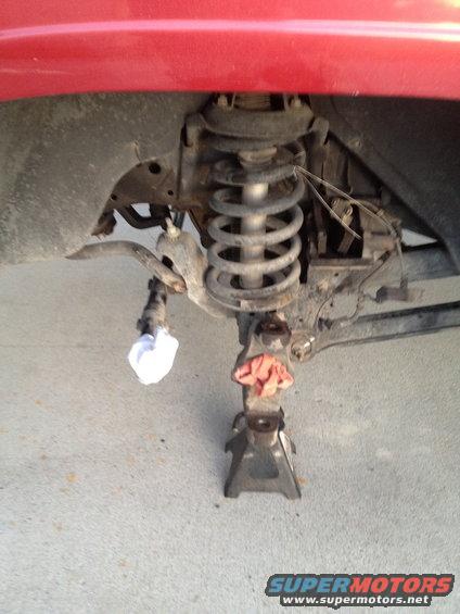 close-up of vehicle's front suspension on jack stands, red body panel visible above