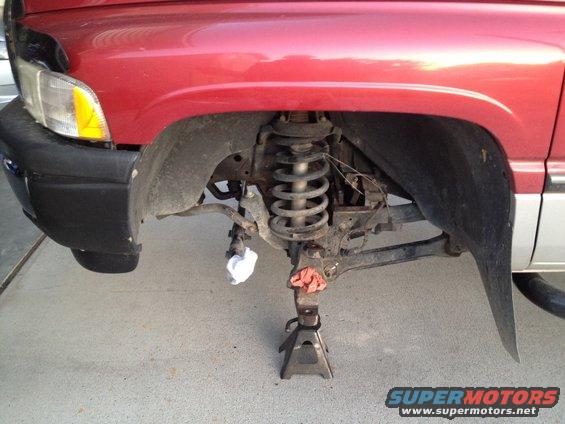 Red pickup truck front suspension on jack stands, showing coil spring and control arms