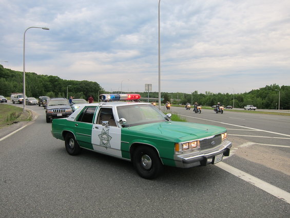 Green and white police car with light bar, driving on a highway with other cars and motorcycles