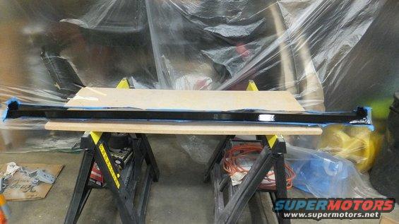 Black bumper on sawhorses, covered in plastic sheeting