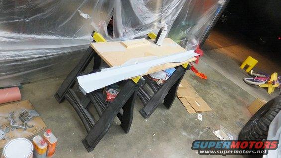 Gray body panel on sawhorses with tools and plastic sheeting