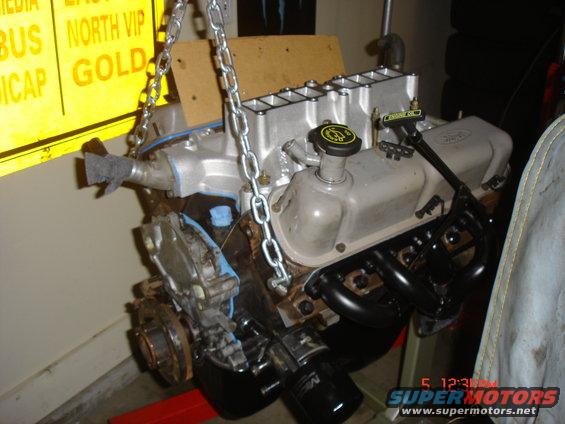 Ford V8 engine assembly hanging from chains, with exhaust manifolds and oil filter visible