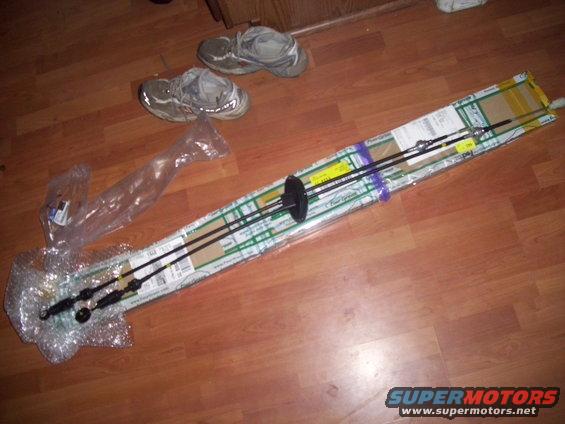 Two black control cables in packaging on a wood floor, with a pair of sneakers in the background