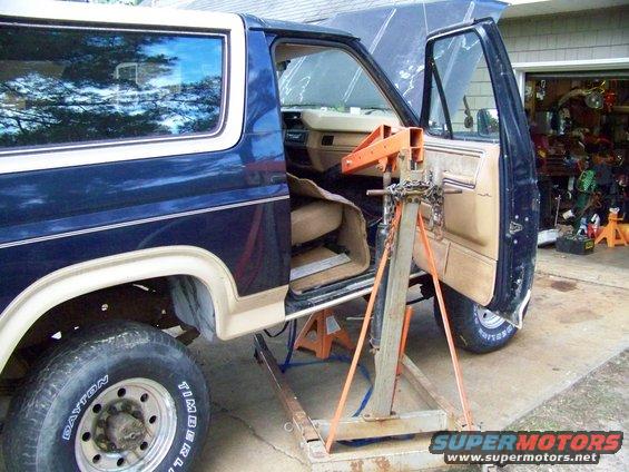 Ford Bronco with doors open, engine hoist positioned inside, jack stands under frame