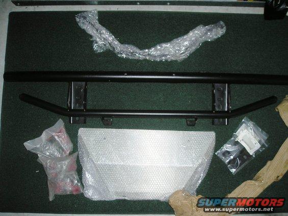 Vehicle bumper and mounting hardware laid out on a dark carpeted surface