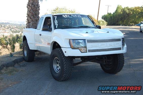 White pickup truck with McNeil sticker on windshield and '707' numbers. It has a custom grille with 'FORD' lettering
