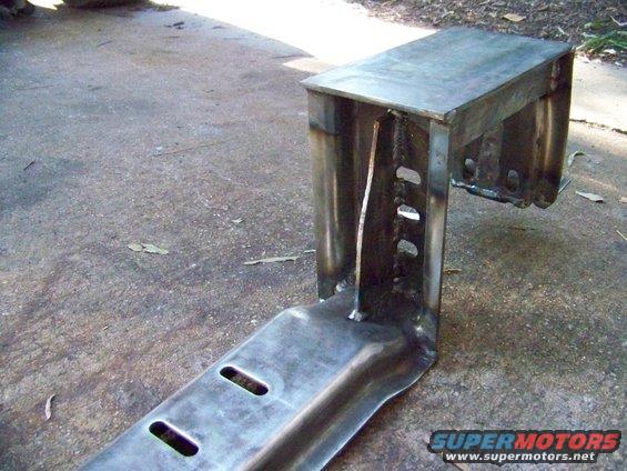 Metal bracket with welded seams and slotted holes, resting on concrete