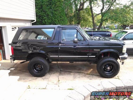 1995 Ford Bronco XLT parked on driveway, side view. Black paint, lifted suspension, aftermarket wheels