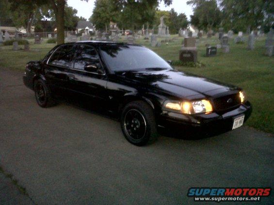 Black Ford Crown Victoria parked on asphalt in a cemetery with tombstones visible