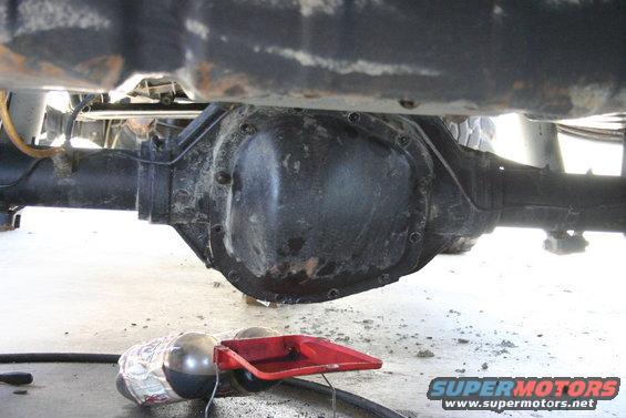 Rear differential assembly with a red oil drain pan and a wrapped object underneath
