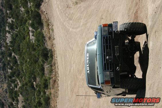 Green Ford Bronco with "ABUSED" text on windshield, parked on dirt road
