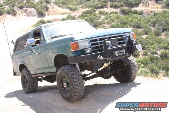 Green 1991 Ford Bronco with aftermarket bumper and winch on a dirt trail