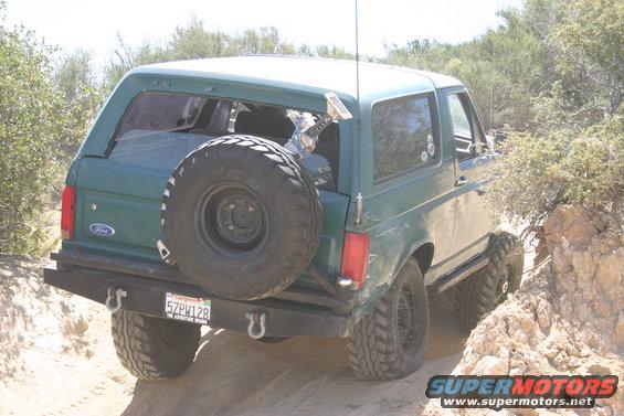 Green 1991 Ford Bronco with spare tire on rear, driving on a dirt trail