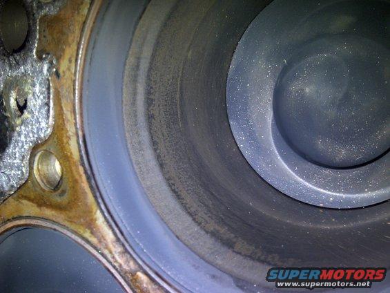 Close-up of an engine cylinder wall with scoring and carbon buildup. Shows part of the engine block casting