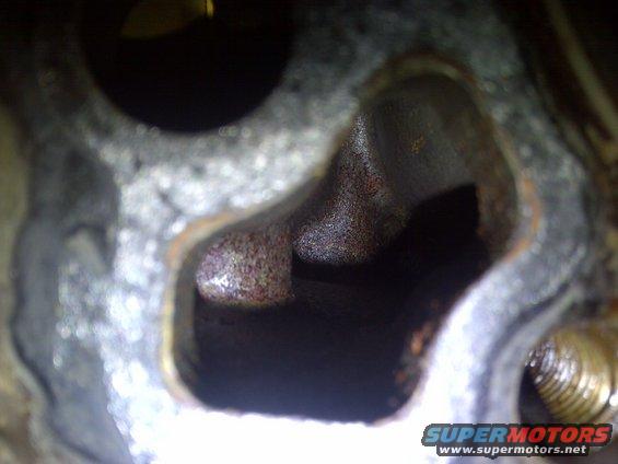 Close-up of a rusted engine cylinder head port with dark interior