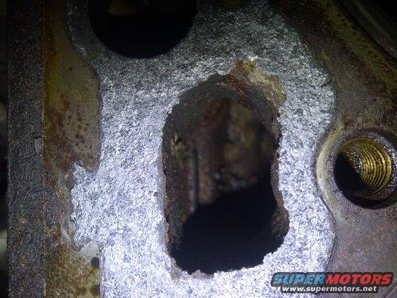 Close-up of a heavily corroded metal engine component with a large hole