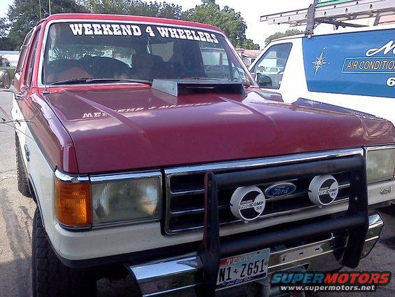 1989 Ford Bronco front view with aftermarket hood scoop and "WEEKEND 4 WHEELERS" windshield banner. Another vehicle is partially visible to the right