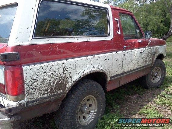1989 Ford Bronco side view, red and white two-tone, covered in mud