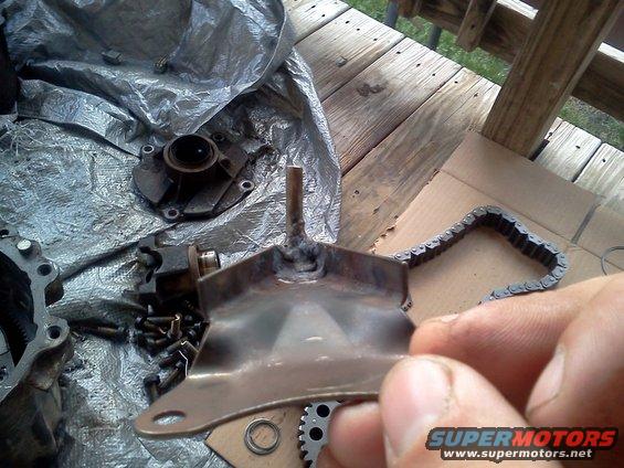 Metal bracket with a welded post held by a hand, next to a roller chain and other disassembled parts