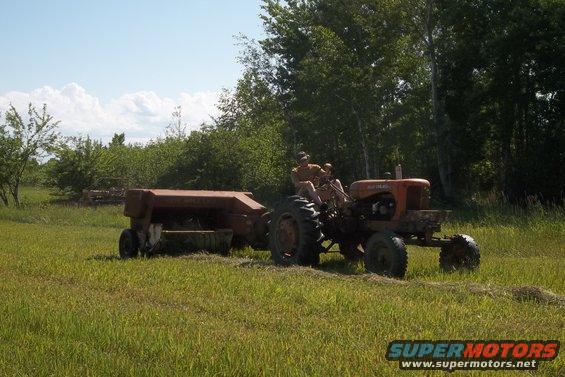 Tractor pulling a baler through a grassy field with two people on the tractor