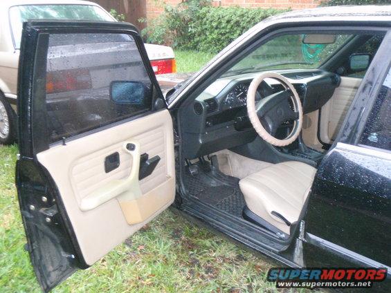 1991 BMW 3 Series interior with beige seats and door panel, black dashboard, and steering wheel. Another BMW is visible outside