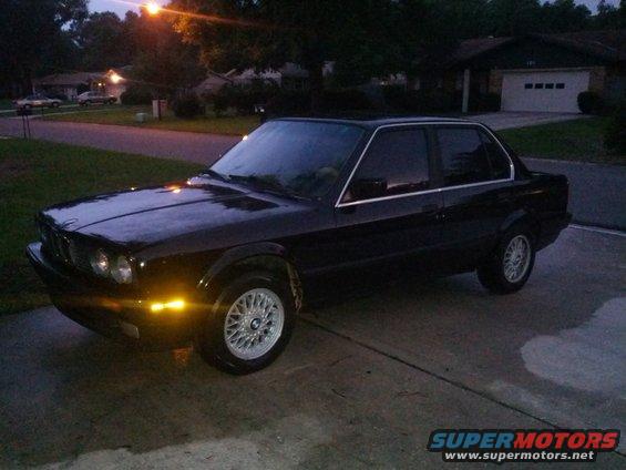 Black sedan parked in a driveway at dusk. It has chrome trim around the windows and silver BBS-style wheels