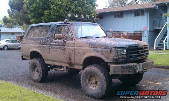 Muddy Ford Bronco parked on street, aftermarket bumper and light bar visible