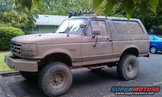Mud-covered 1992 Ford Bronco with aftermarket bumper and roof lights, viewed from the front-left