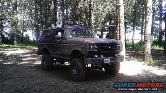 1995 Ford Bronco lifted with off-road tires parked in a wooded area