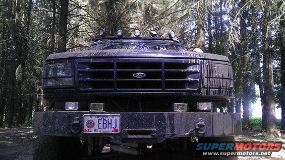 Front view of a muddy Ford F-Series truck with a winch and roof lights parked in a forest