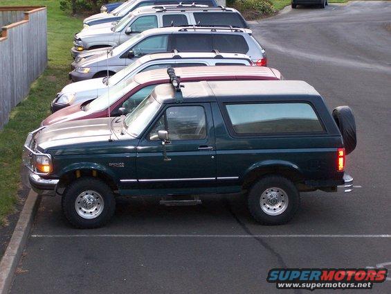 Dark green Ford Bronco parked in a lot, side view. Spare tire mounted on rear door