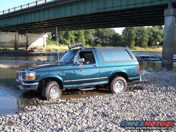 Teal 1995 Ford Bronco with roof lights driving through a rocky riverbed
